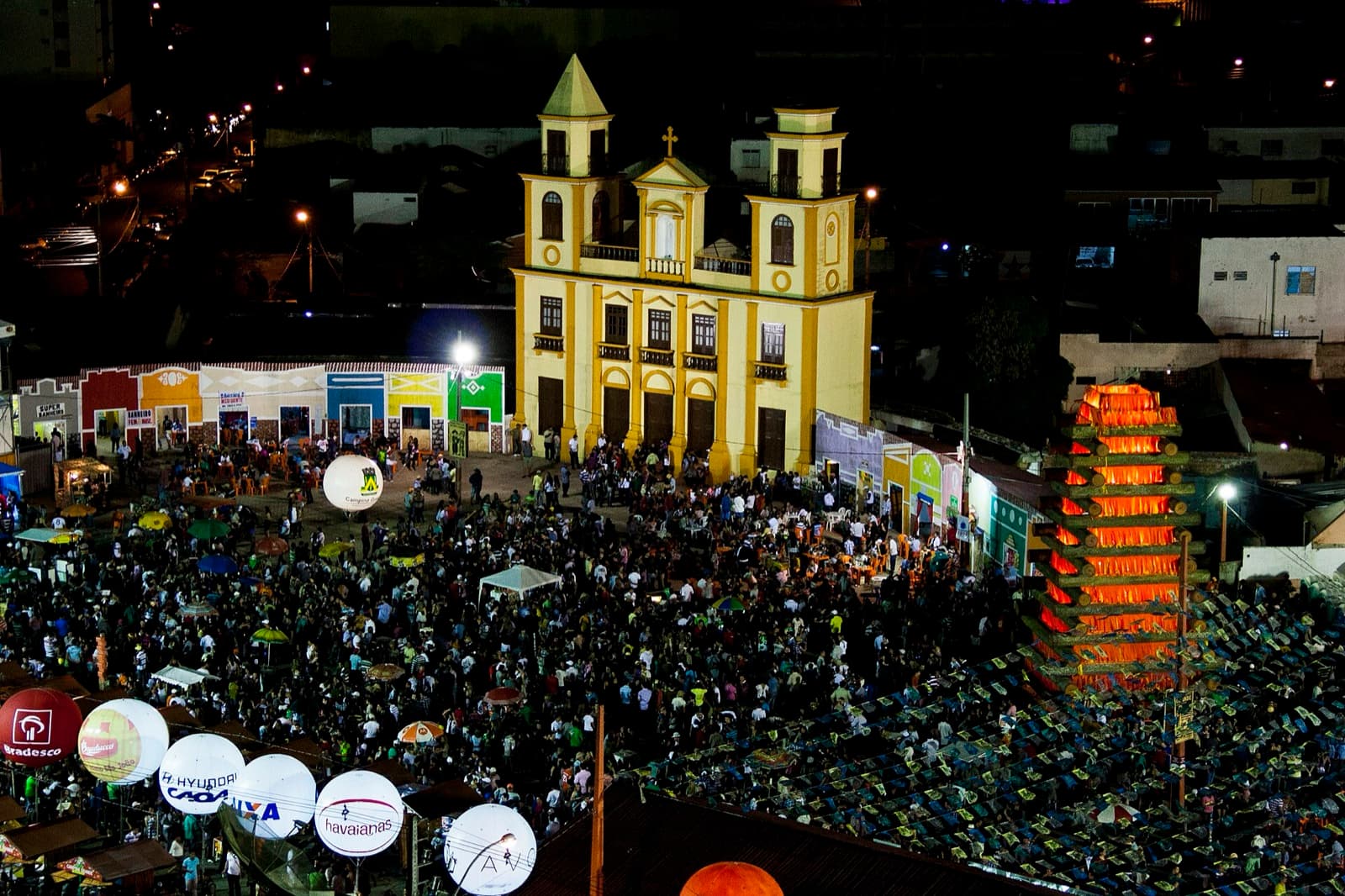 Fogueira de São João com bandeirinhas coloridas ao fundo, cenário típico de festa junina nordestina